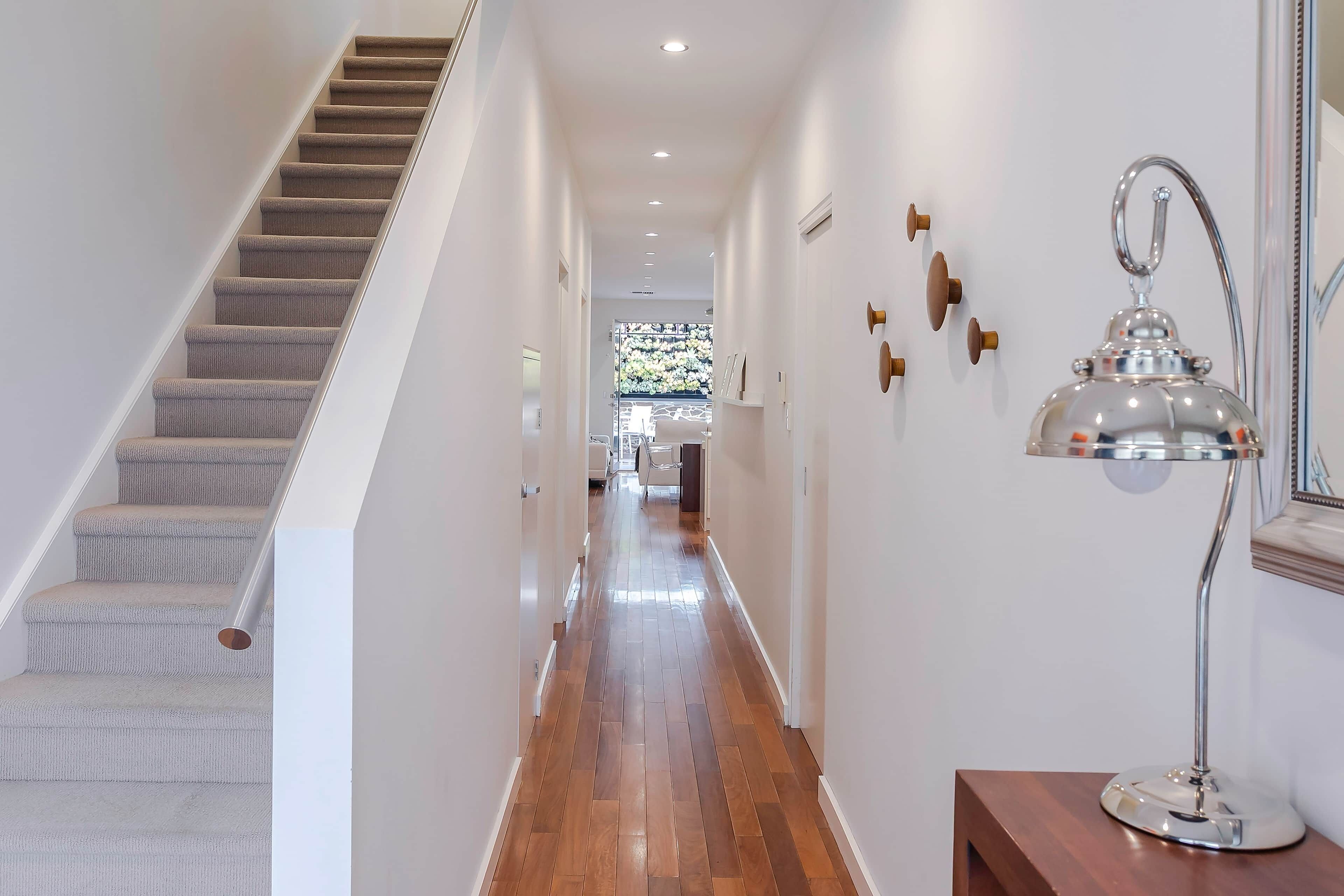 A modern hallway with a carpeted staircase, wooden flooring, and a wall-mounted lamp.