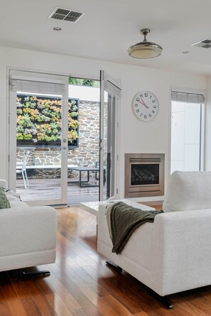 Ein modernes Wohnzimmer mit Kamin, einer Uhr und Blick auf einen Garten durch Glastüren.