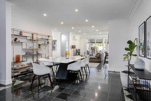 A modern kitchen with a dining area, featuring a marble floor, white walls, and a central island.