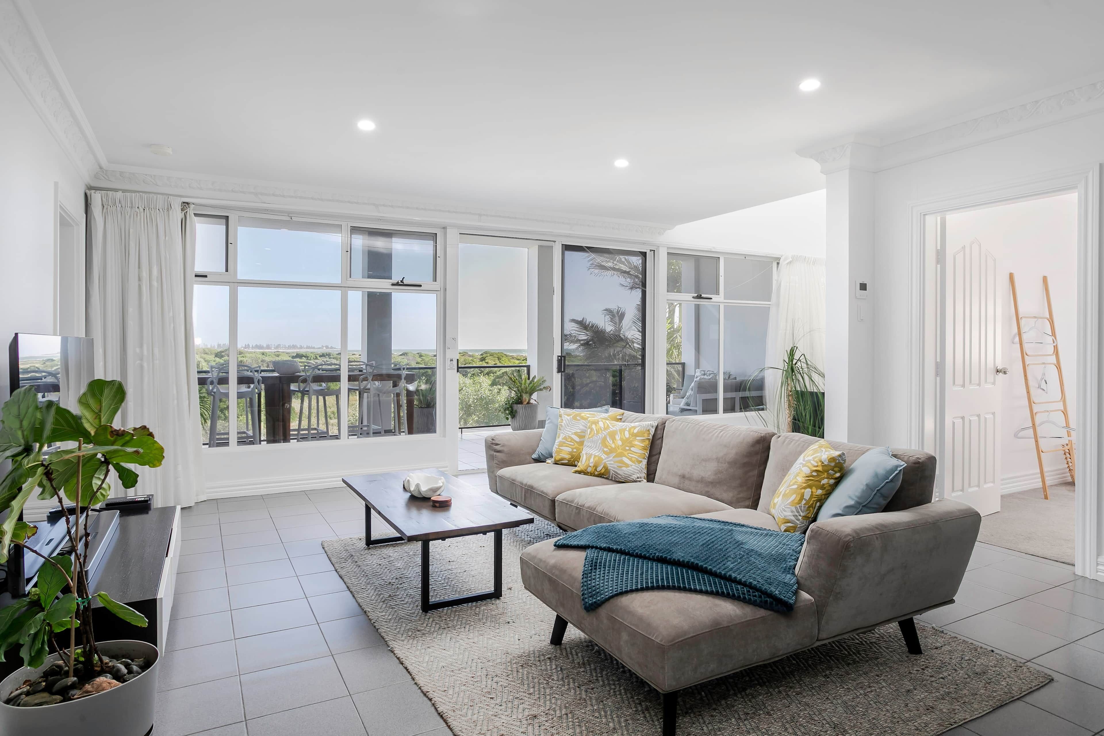 A spacious living room with a sofa, coffee table, and large windows offering a view of the outdoors.