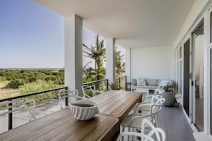 A balcony with a wooden table, white chairs, a sofa, and a potted plant. - Ocean View Adelaide Escape - North Haven (North Haven)