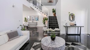 Un interior moderno con una escalera, un sofá blanco, una mesa redonda con una planta y un suelo de baldosas blanco y negro.