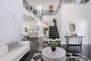 A modern interior with a staircase, a white sofa, a round table with a plant, and a black and white tiled floor. - Ocean View Adelaide Escape - North Haven (North Haven)
