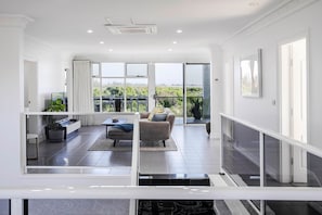 A spacious living area with a balcony, a sofa, a coffee table, and a TV. - Ocean View Adelaide Escape - North Haven (North Haven)