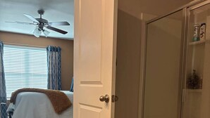 Ein Schlafzimmer mit einem Bett, einem Deckenventilator und einer Tür zu einem Badezimmer mit Duschkabine.