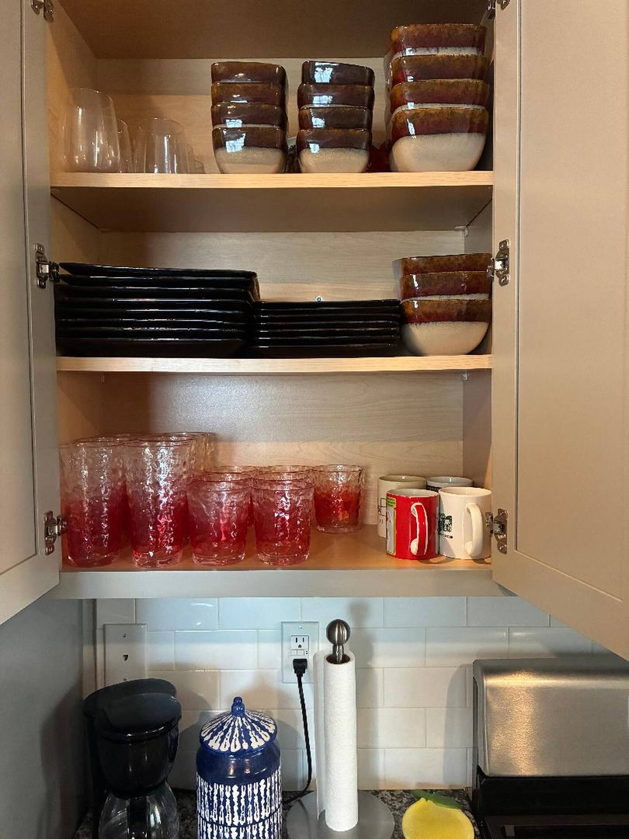 A kitchen cabinet with shelves holding glassware, plates, and mugs.