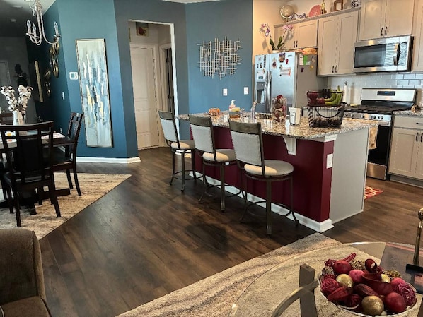 A modern kitchen with a central island, stainless steel appliances, and a dining area with a dark wood floor. - 3BR Townhouse 3 min to I-20, Exit 11 (Graniteville)