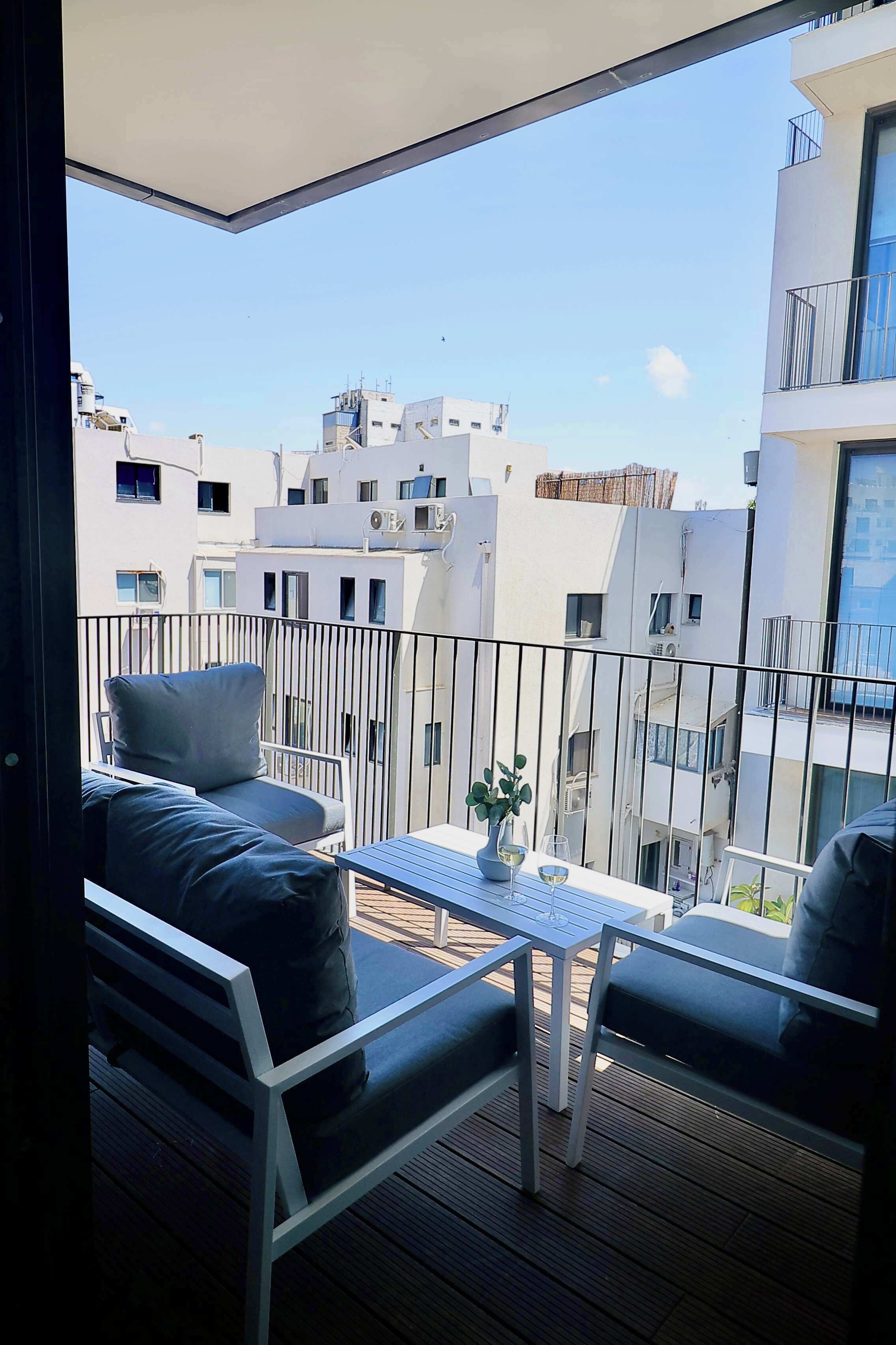 A balcony with a table and seating, overlooking a cityscape with modern buildings.