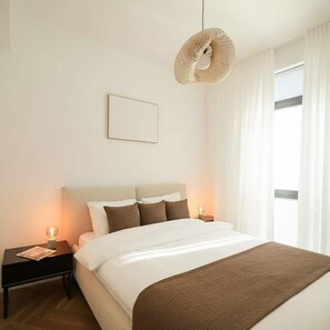 Ein Schlafzimmer mit Bett, Nachttischen, einer Hängelampe, einem Fenster mit Vorhängen und einem gerahmten Bild an der Wand.