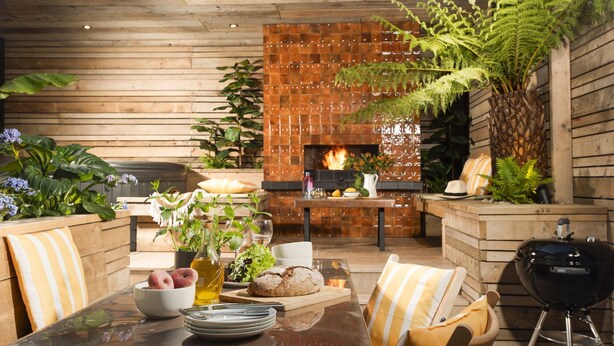 A dining area with a wooden table, chairs, a grill, and a brick wall with a fireplace. - Sandy Boobies - Garden, Hot tub, Dog friendly (St Ives)