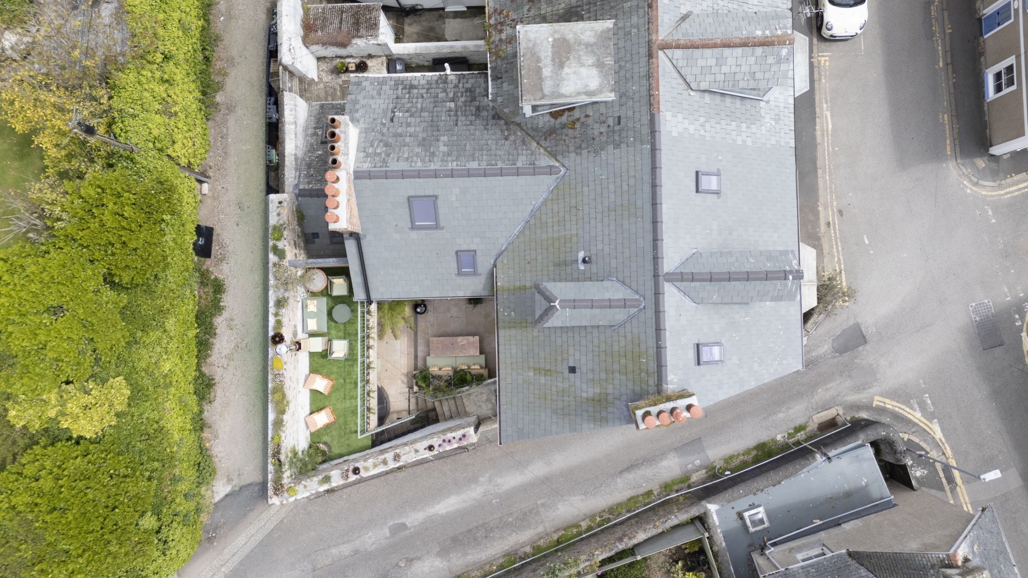 Une vue aérienne d’un bâtiment doté de plusieurs toits, d’une cour pavée avec des espaces de repos extérieurs, et d’une rue adjacente à la propriété.