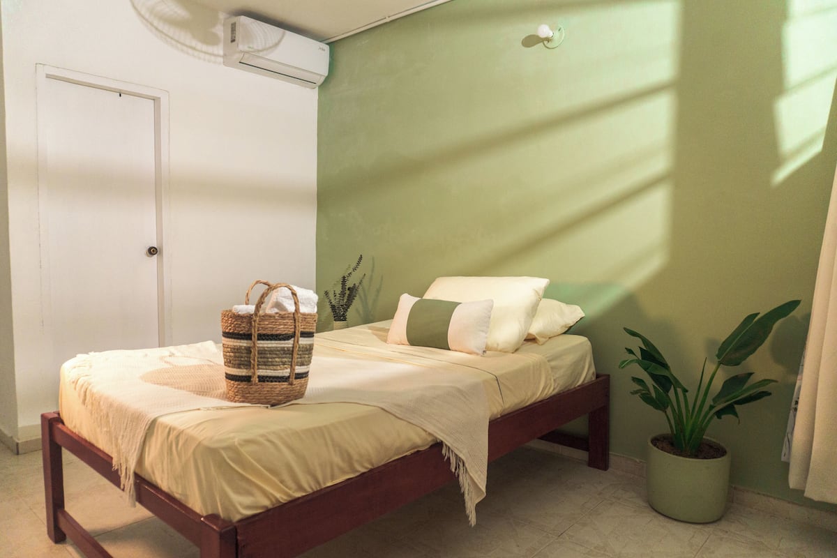 Un dormitorio con cama, una cesta junto a la cama, una planta en maceta y una puerta.