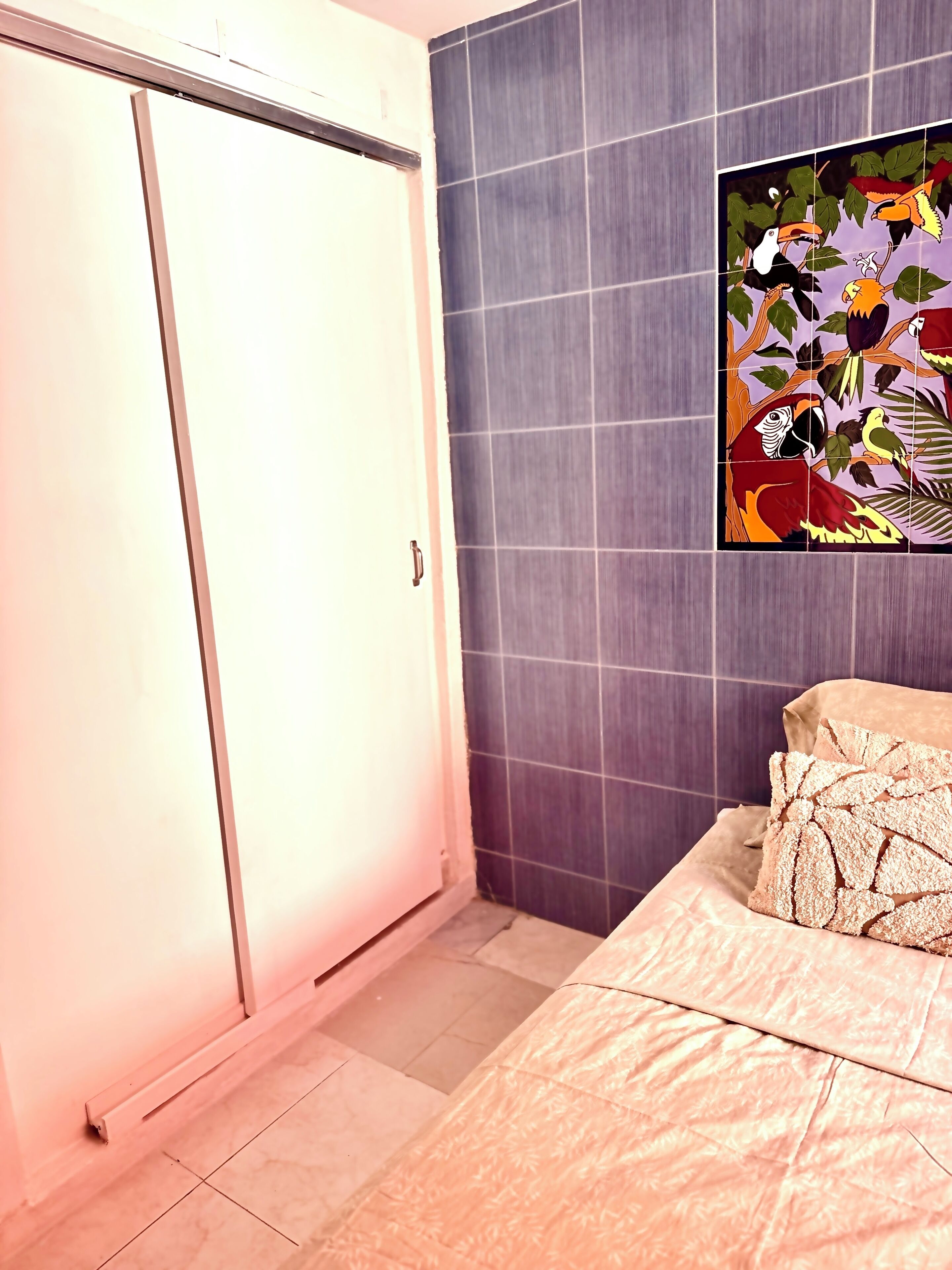 Un dormitorio con cama, puerta corredera, pared con diseño de azulejos y un cuadro enmarcado.