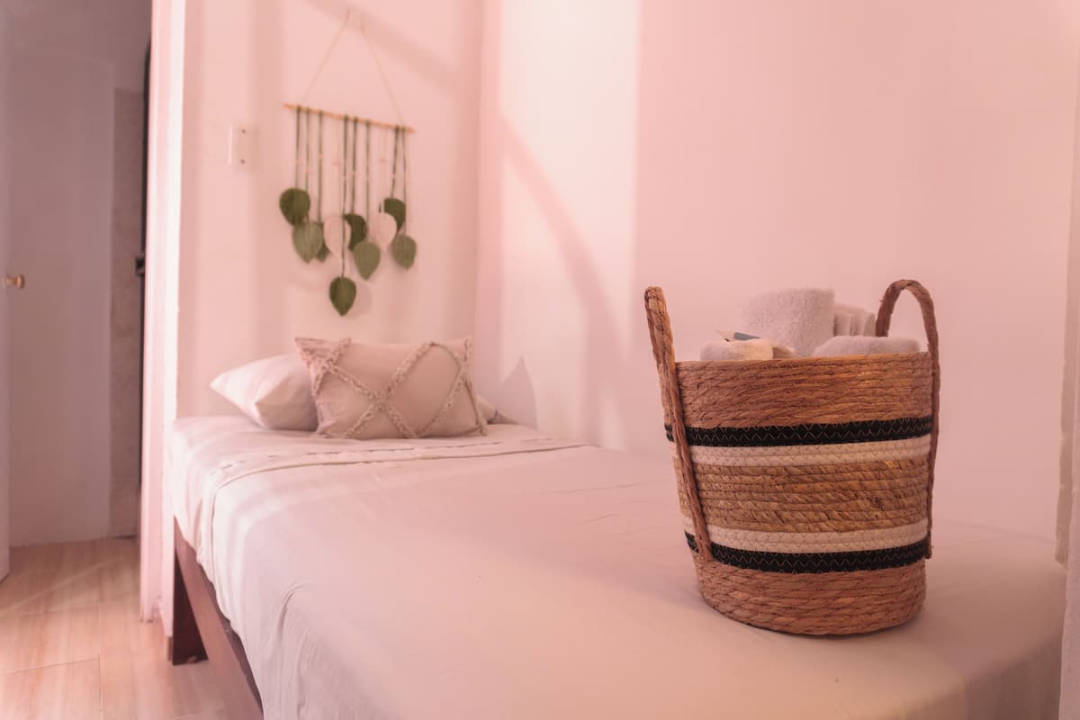 Un dormitorio con una cama, una cesta tejida y una planta en la pared.