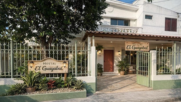 Ein Hotel Eingang mit einem Schild, auf dem 'HOSTAL El Guayabal' steht, einem verschlossenen Tor und einem Weg zum Eingang.