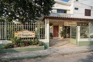 L’entrée d’un hôtel, avec une enseigne indiquant « HOSTAL El Guayabal », une porte grillagée et un chemin menant à la porte d’entrée.