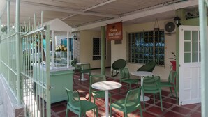 Ein überdachter Außenbereich mit grünen Stühlen und Tischen, einem Schild für 'Casa Guayabal Hostel & Cocina' und einem Fenster mit Gitterstäben.