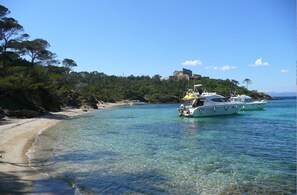 Ein Strand mit klarem Wasser, Booten und einem Gebäude auf einem Hügel.