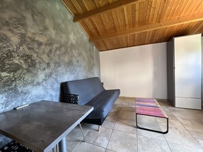 Una stanza con una parete in cemento, un soffitto in legno, un divano nero, un tavolino e una panca colorata.