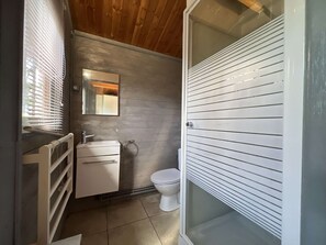 Un baño pequeño con techo de madera, un lavabo blanco, un inodoro y una cabina de ducha con mampara de vidrio.