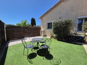 Eine Terrasse mit rundem Tisch und Stühlen, einem Holzzaun und einem Gebäude mit einem Fenster.