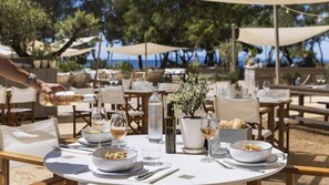 Un área de comedor al aire libre con mesas, sillas y sombrillas, con vista a la playa.