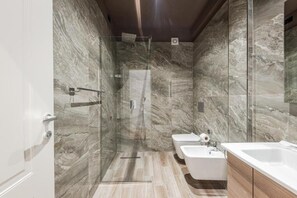 Un bany modern amb dutxa de vidre, un lavabo blanc i un mirall gran.