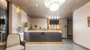 A reception desk with a sign reading 'Relaxinn Hotel,' a chair, a water dispenser, and a chandelier. - Relax Inn Hotel (Durrës)