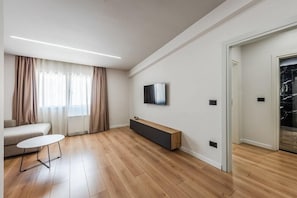 A modern living room with a sofa, a coffee table, a TV mounted on the wall, and a wooden bench. - Relax Inn Hotel (Durrës)