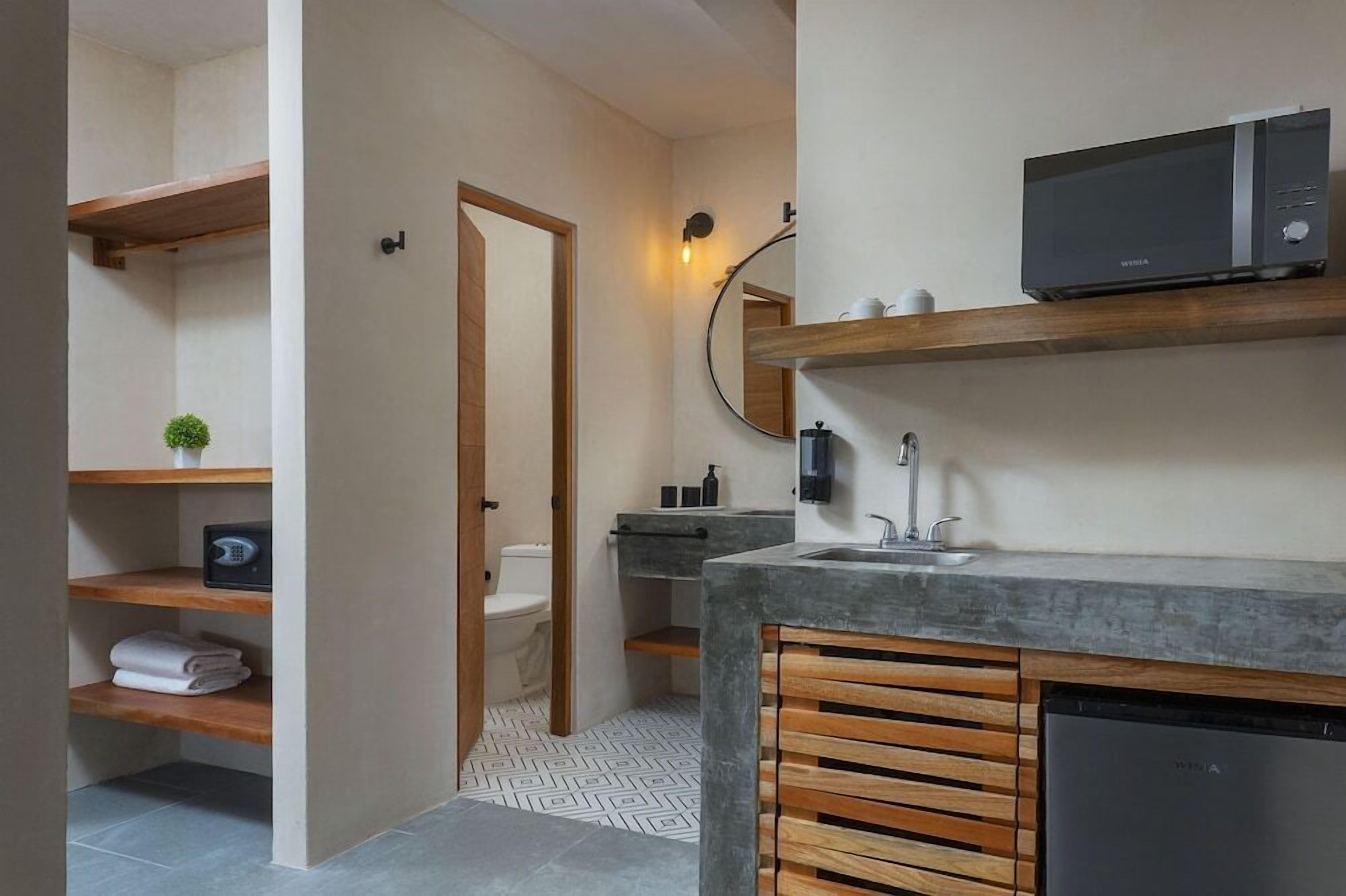 Une salle de bain moderne équipée de toilettes intégrées, d’un lavabo, d’un four à micro-ondes et d’une étagère en bois où sont rangées des serviettes.
