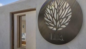 A modern building entrance with a circular sign featuring a tree design and the letters 'LLX' below it. - Illa Boutique Hotel Cozumel (Cozumel)