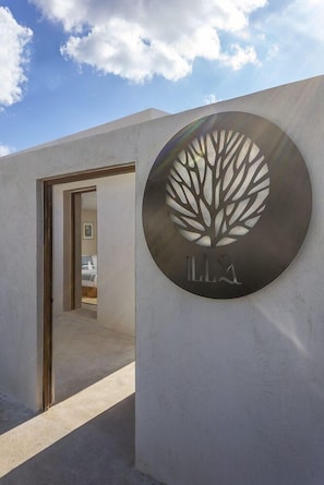 A modern building entrance with a circular sign featuring a tree design and the letters 'LLX' below it. - Illa Boutique Hotel Cozumel (Cozumel)