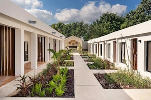 A modern hotel corridor with a central pathway, surrounded by lush greenery and white walls. - Illa Boutique Hotel Cozumel (Cozumel)