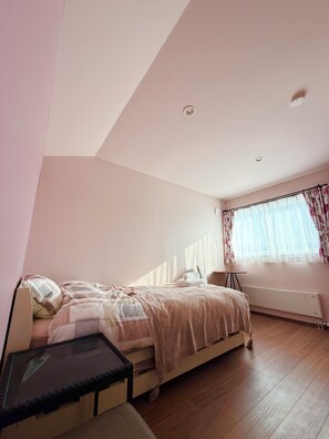Um quarto com cama, uma mesinha, um radiador e uma janela com cortinas.