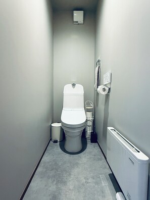 Um banheiro pequeno com vaso sanitário, lixeira, radiador e porta-toalhas.