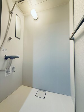 Ein kleiner, weiß gefliester Duschbereich mit Duschbrause, Wandspiegel und Toilette.