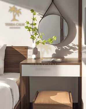 Um quarto moderno com cabeceira de madeira, mesa de cabeceira com um vaso branco e uma planta, espelho redondo e cama com roupa de cama branca.