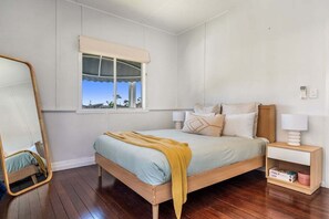 A bedroom with a bed, bedside tables, a mirror, and a window with a view.
