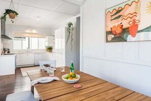 Eine moderne Küche mit weißen Schränken, einem Essbereich mit Holztisch und einer hängenden Pflanze.