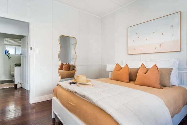 A bedroom with a bed, a mirror, a painting, and a door leading to a bathroom.