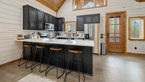 A kitchen with dark wood cabinets, a stainless steel refrigerator, and a bar area with stools. - Couples Retreat w/ Hot Tub, Jacuzzi, Fireplaces (Broken Bow)