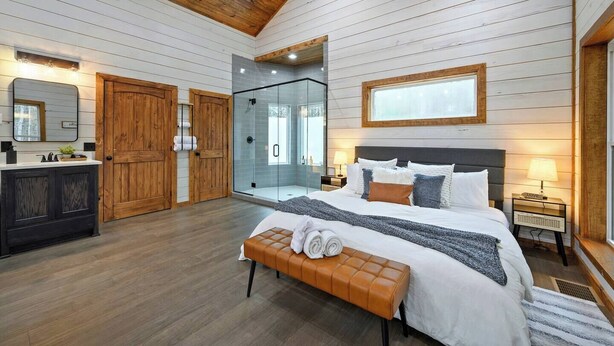 A bedroom with a bed, bench, bedside tables, and a glass-enclosed shower. - Couples Retreat w/ Hot Tub, Jacuzzi, Fireplaces (Broken Bow)
