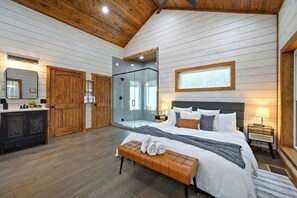 Ein Schlafzimmer mit Bett, einer Sitzbank, Nachttischen und einer Duschkabine aus Glas.