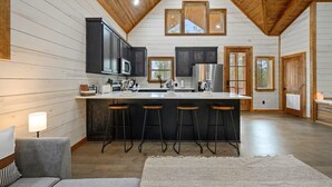A kitchen with a central island, bar stools, and a high ceiling with wooden beams. - Couples Retreat w/ Hot Tub, Jacuzzi, Fireplaces (Broken Bow)