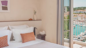 Een hotelkamer met een bed, kussens, een vaas en uitzicht op een jachthaven.