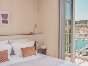 A hotel room with a bed, pillows, a vase, and a view of a marina. - Hotel Liautaud (Cassis)