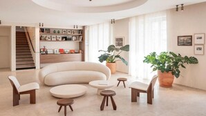 Een moderne woonkamer met een gebogen bank, ronde salontafels en een trap die naar een ander niveau leidt.