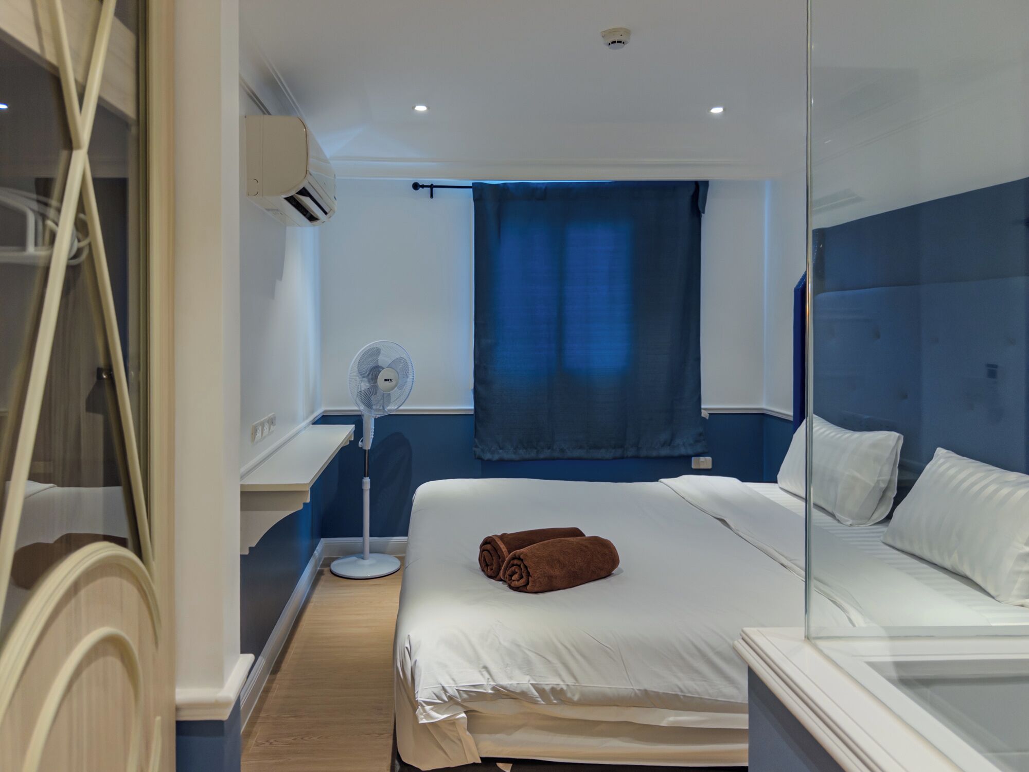 Une chambre d’hôtel équipée d’un lit, d’un ventilateur sur pied, d’une fenêtre avec des rideaux et d’un appareil de climatisation.