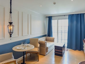Ein Zimmer mit einem runden Tisch, zwei Stühlen, einer Couch, einer Pendelleuchte und einem Fenster mit Vorhängen.