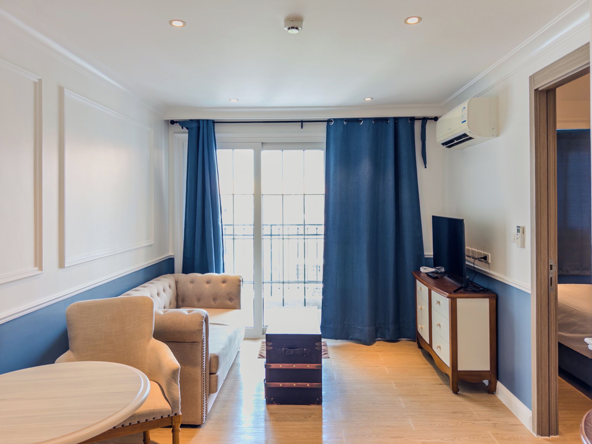 A modern living room with a sofa, a round table, a TV, and a balcony with blue curtains.